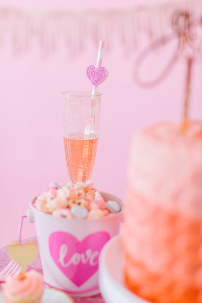 Galentine's Day Party idea featuring conversation heart popcorn and pink sparkling rose with paper heart straw.
