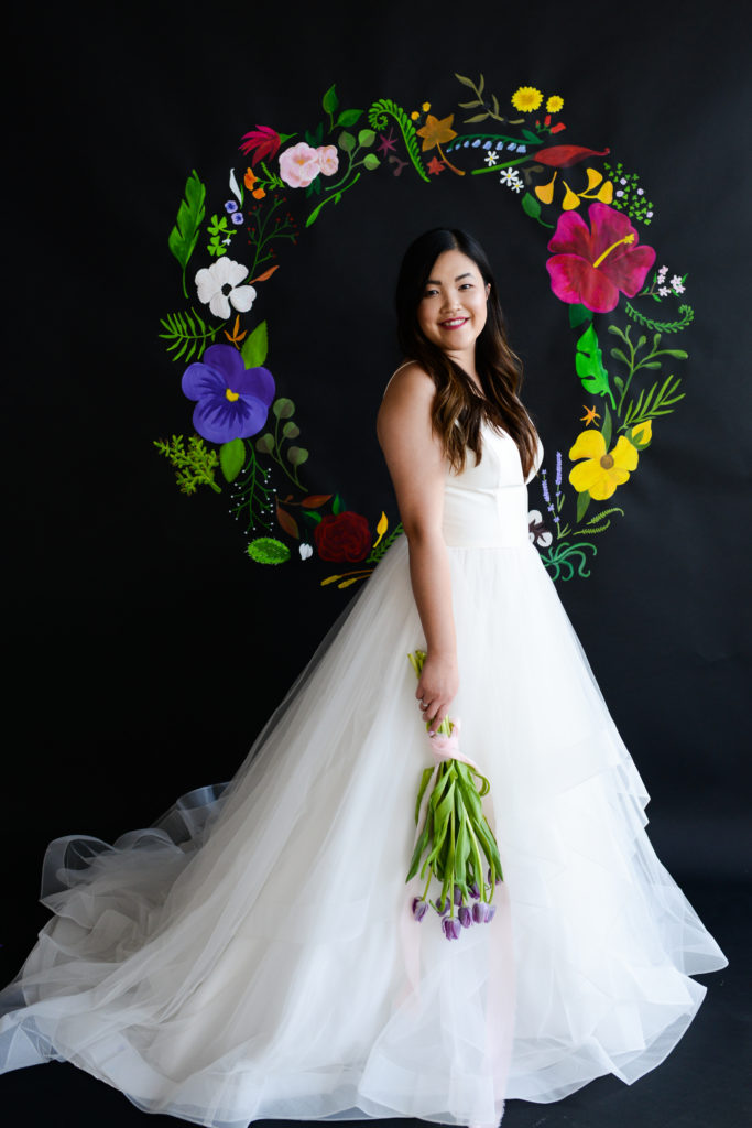 Model in A-line bridal gown in front of painted floral backdrop on black paper