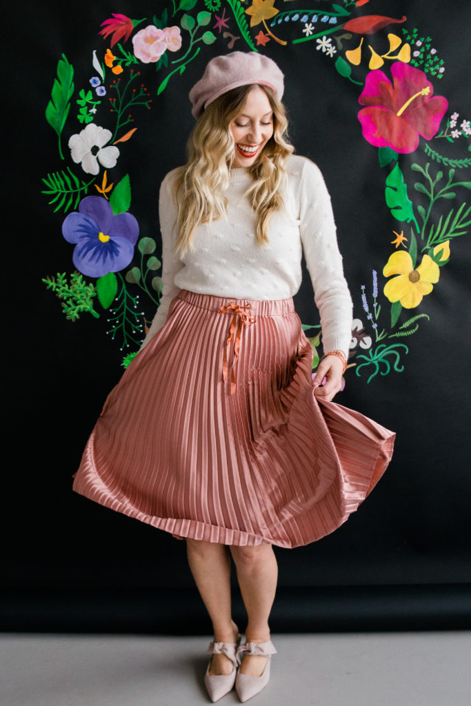 Model dancing in pleated skirt front of painted floral backdrop on black paper