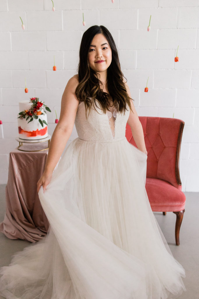 Valentine's day bridal inspiration featuring coral tulip backdrop, two-tiered cake and velvet chair.