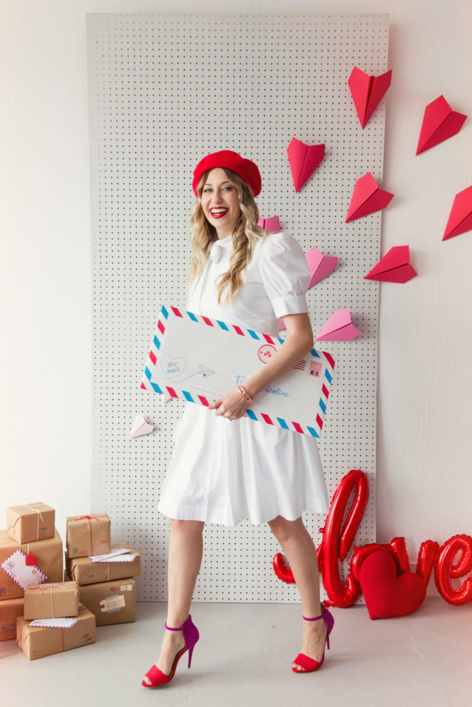 Valentine's Day photo shoot inspiration featuring model holding giant envelope and paper plane backdrop