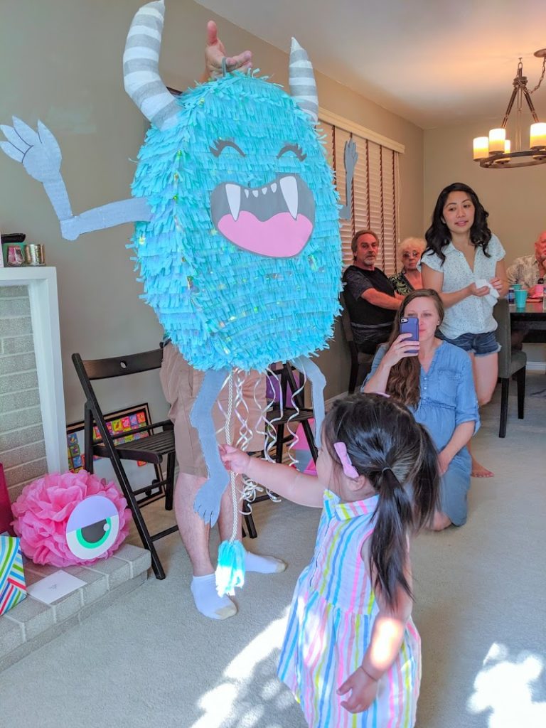 Birthday girl pulling string on cute turquoise monster pinata