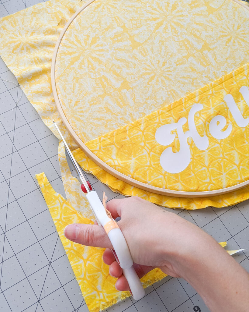 Trimming the extra fabric around embroidery hoop using scissors