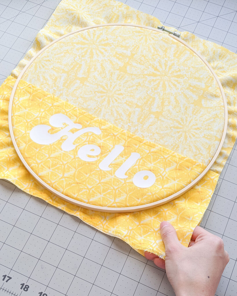 Pulling edges of yellow fabric around embroidery hoop