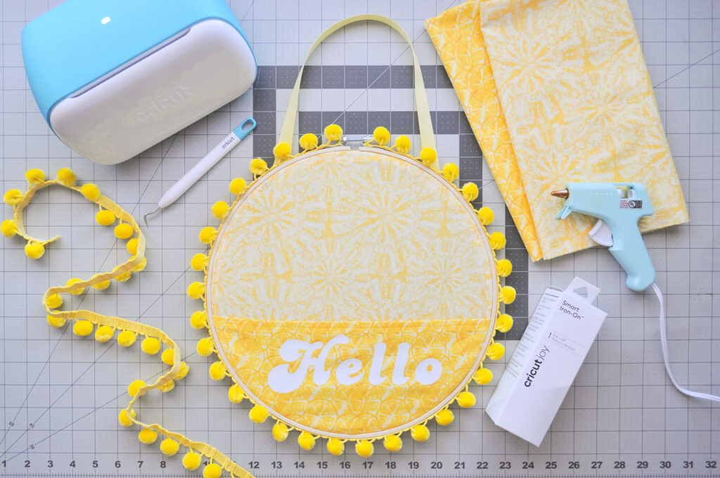 Overhead shot of Cricut Joy, sunshine wreath, fabric, trim and Smart Iron-On