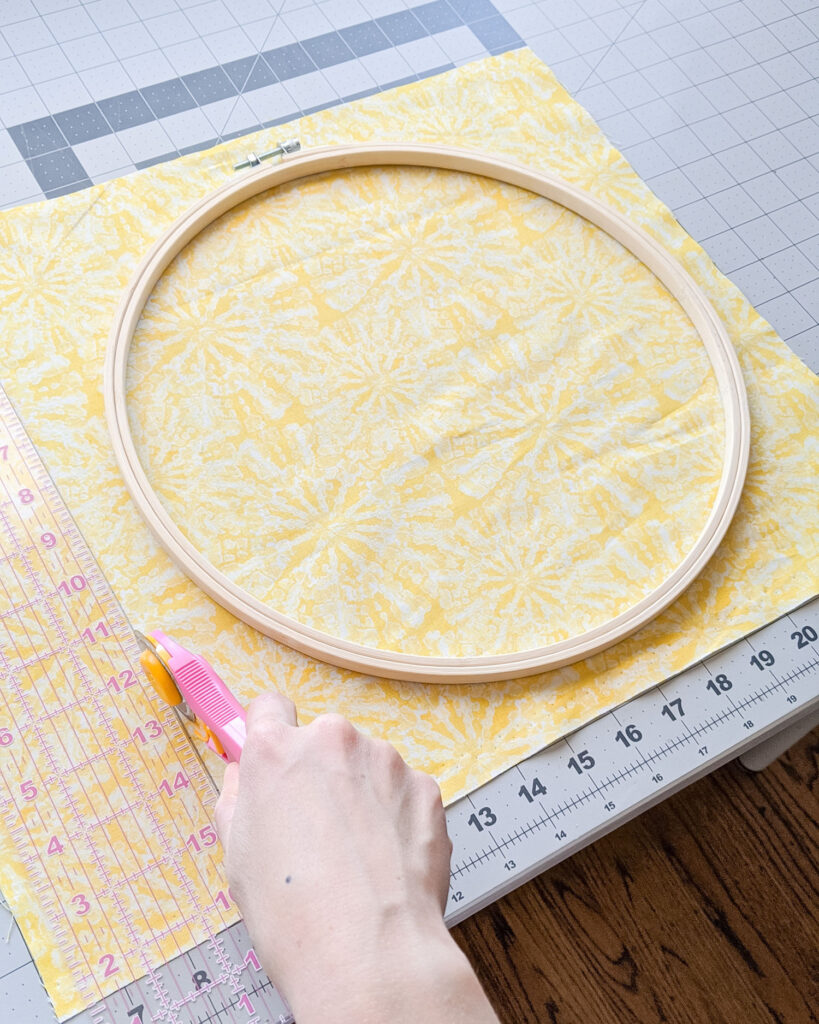 Crafter cutting the extra fabric around embroidery hoop