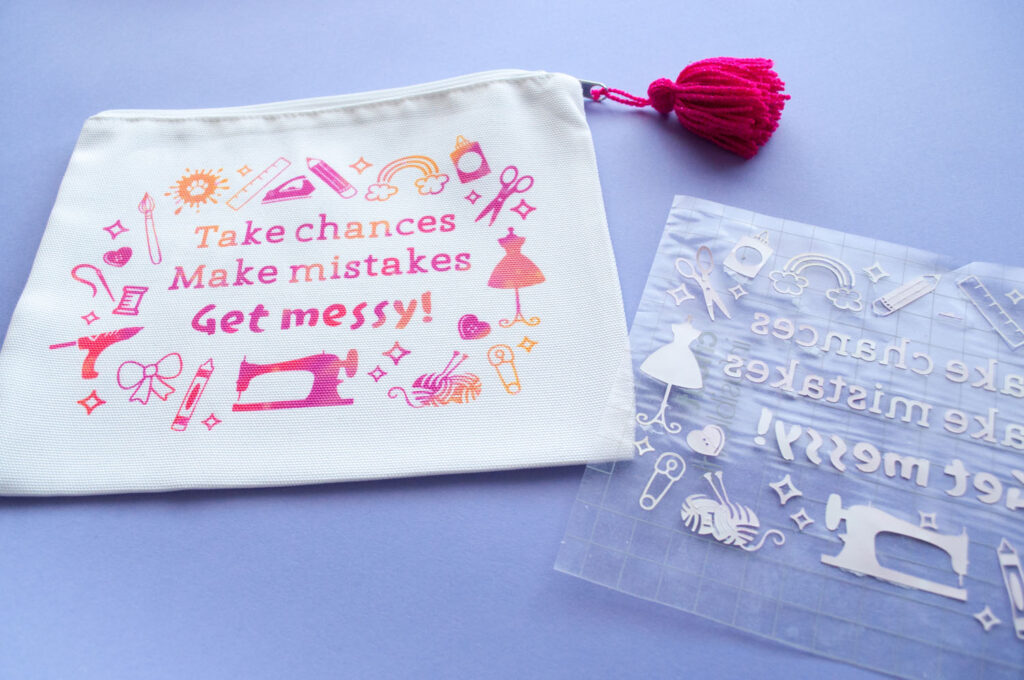 Close up of craft supplies bag. Design has various craft supplies and says "Take chances, make mistakes, get messy!" Next to it is a used transfer sheet