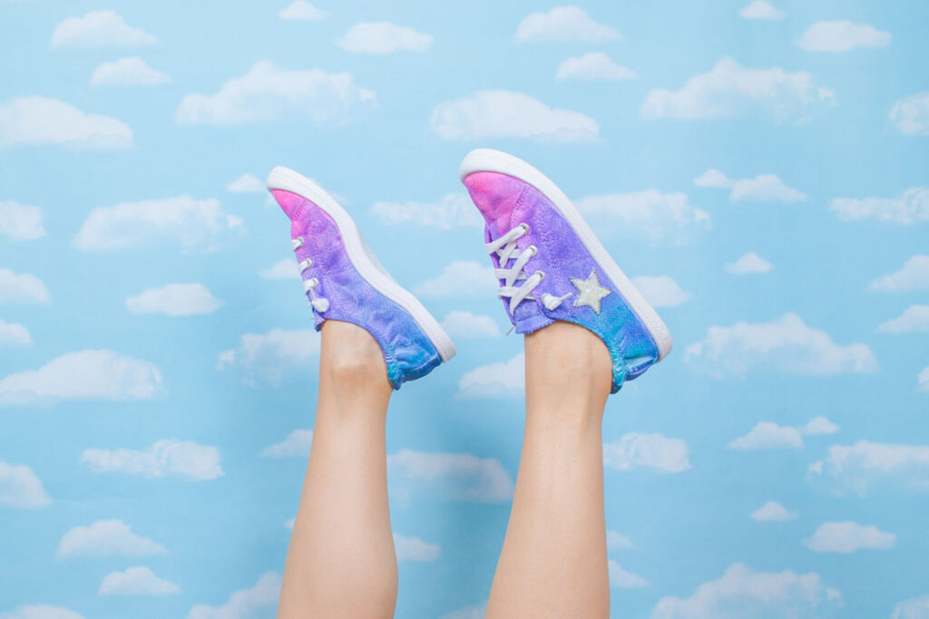 Tie dyed shoes and legs up in the air in front of cloud background