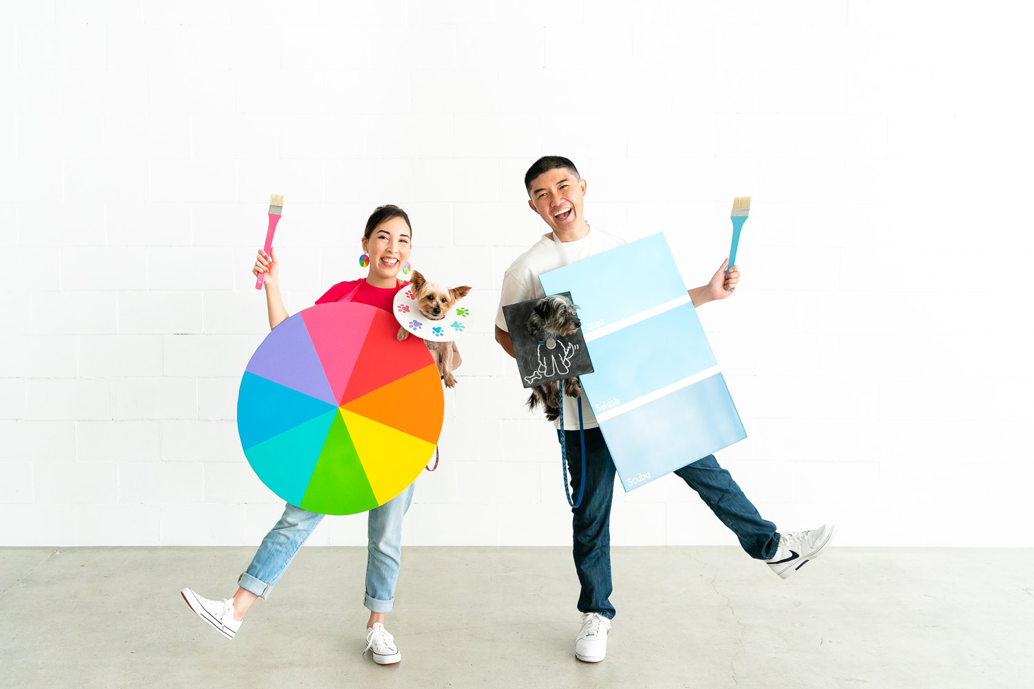 Couple wearing color wheel and paint chip costume holding dogs in paint palette and doodle costume