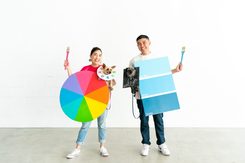 Color wheel and paint chip part of colorful family costume Couple holding dogs dressed as paint palette and a doodle.