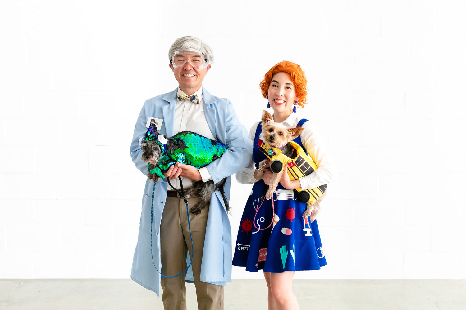 Couple dressed as Bill Nye and Ms. Frizzle. Dogs dressed as chameleon and school bus. Part of Magic School Bus costume.