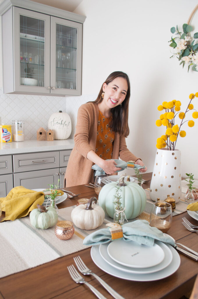 Blaire from Freshly Fuji setting her Thanksgiving table. She's holding a blue cloth napkin.