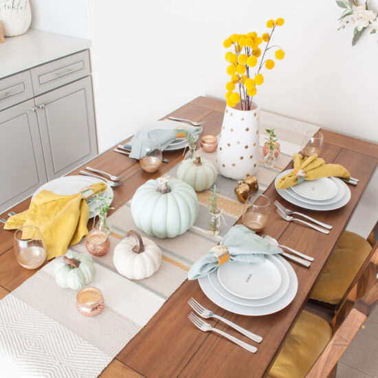 Casual Thanksgiving table featuring pumpkin centerpiece and light blue and mustard Fall decor.