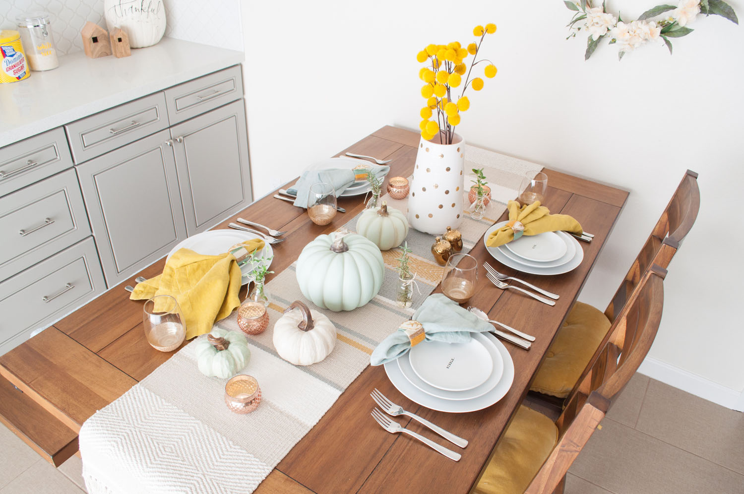 Casual Thanksgiving table featuring pumpkin centerpiece and light blue and mustard Fall decor.