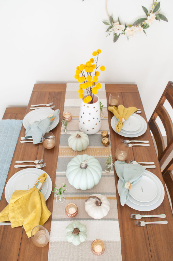 Thanksgiving table with pumpkin centerpiece. The color scheme is light aqua blues and mustards.