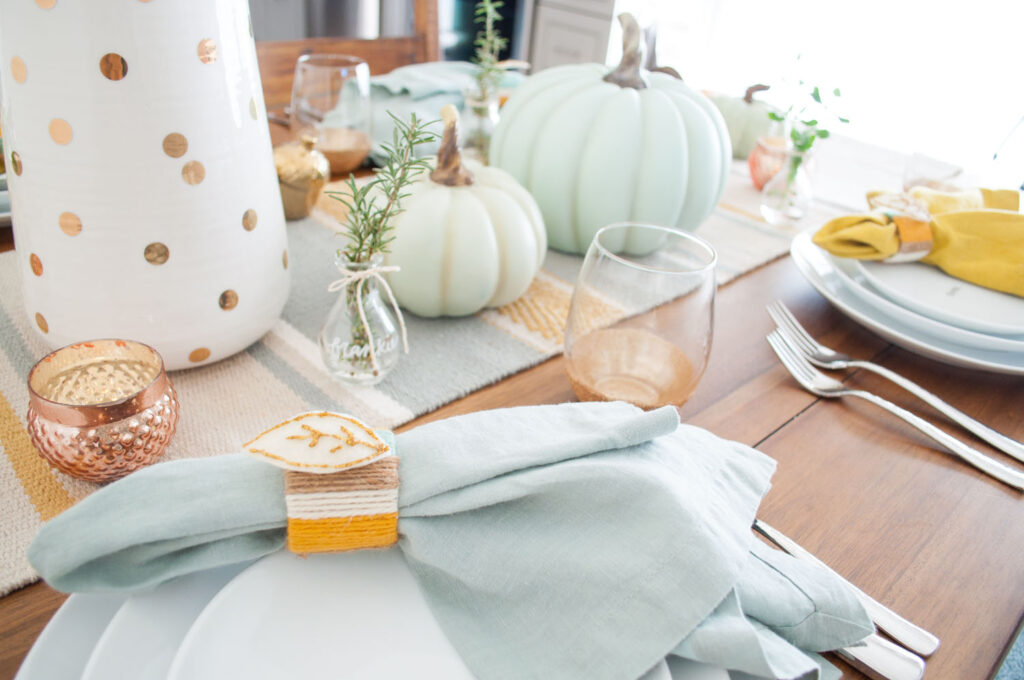 Close up of handmade napkin ring made with yarn and felt. The napkin ring is placed on an aqua linen napkin and placed on white plates.