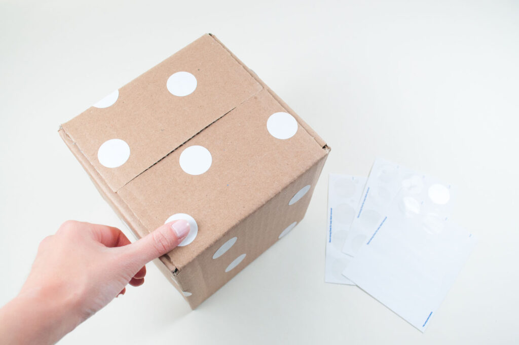 Placing white dot stickers on brown cardboard box.