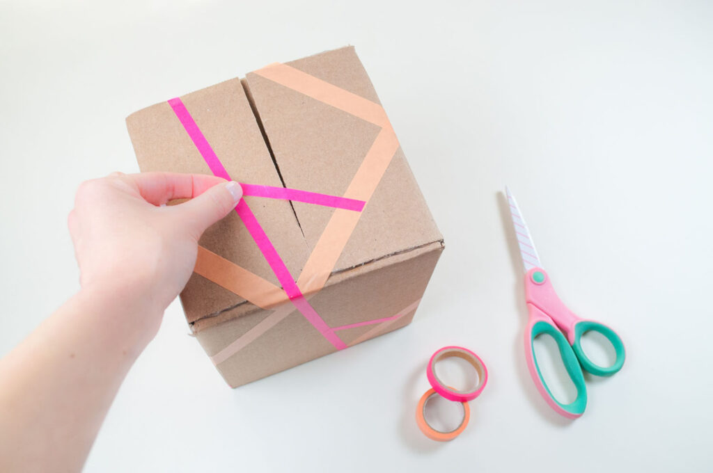 Placing washi tape of various thicknesses on brown cardboard box.