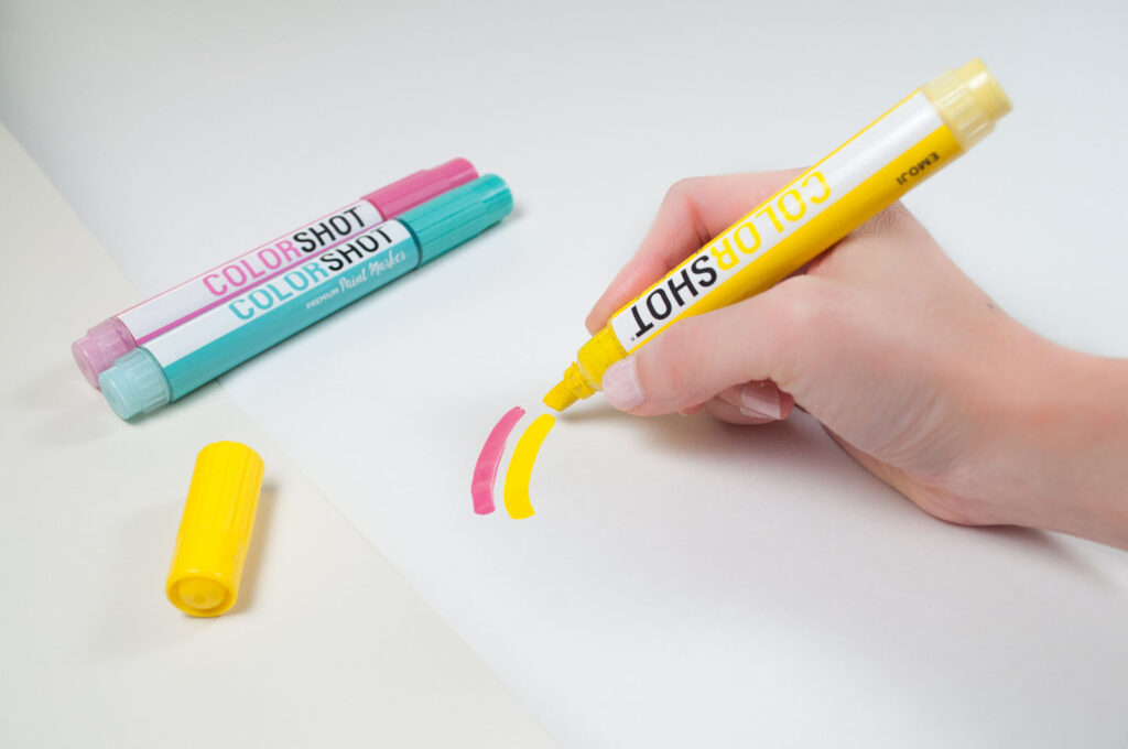 Using Emoji paint marker to draw second rainbow brush stroke on white gift wrap.