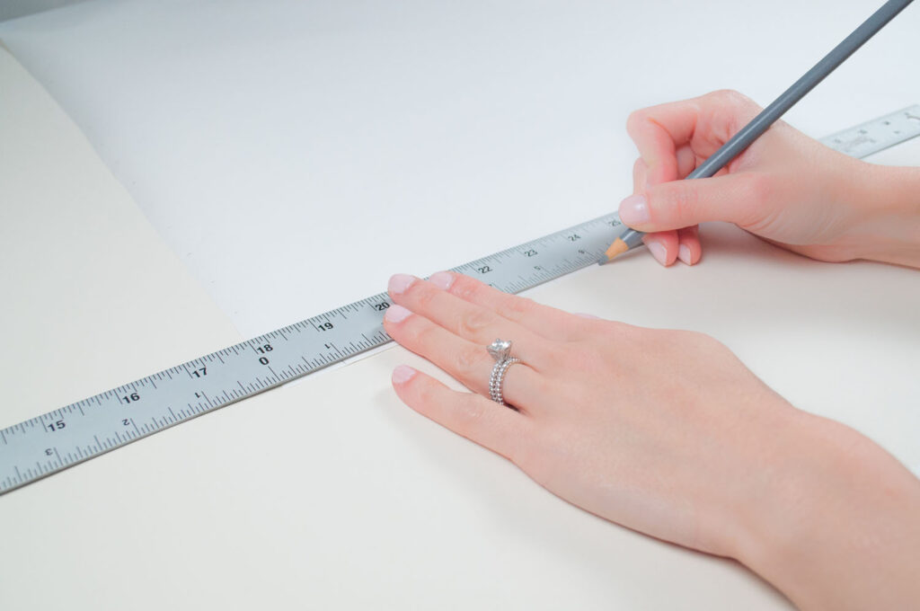 Drawing 1 inch markings along vertical and horizonal edges of the white gift wrap to prepare for hand drawn grid design.