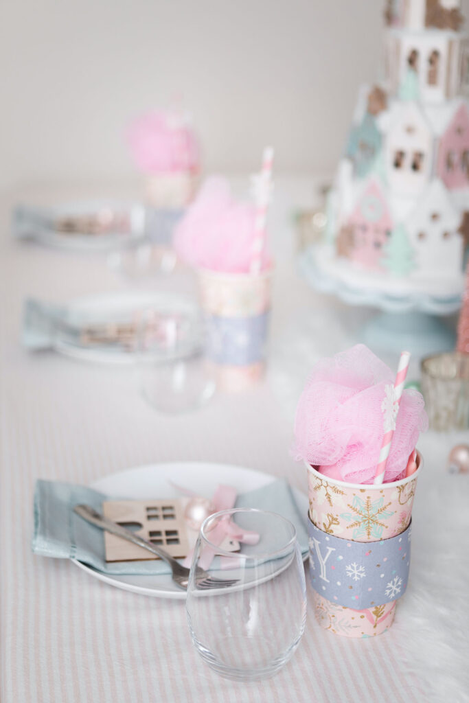 Pink Christmas tablescape view from the side. There are 3 place settings with silvery blue napkins and pink holiday cup favors.