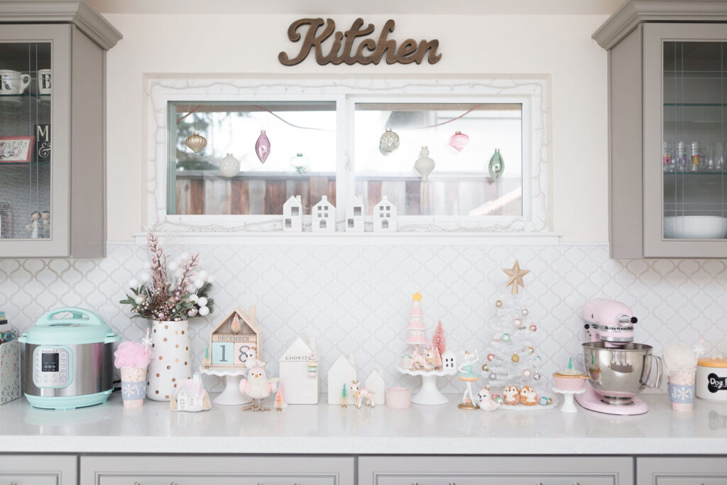 Pink Christmas kitchen display featuring animal figurines, trees and houses. The color palette is white, light pink and mint blue.