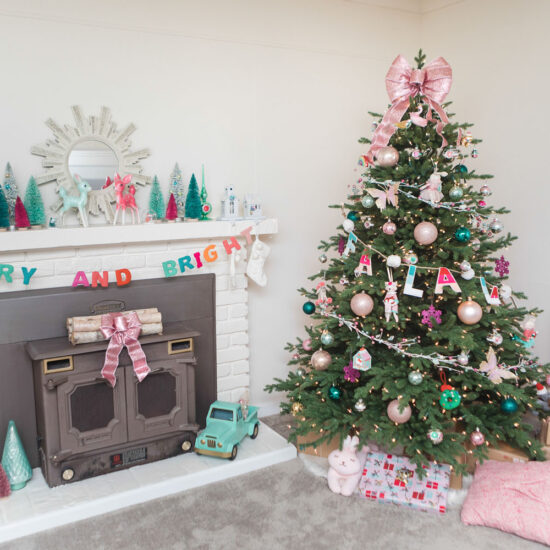 Living room with cream walls decorated for Christmas. The fireplace mantel is decorated with colorful bottle brush trees and a "Merry and Bright" garland. The tree is decorated with colorful ornaments and is topped with a giant pink bow.