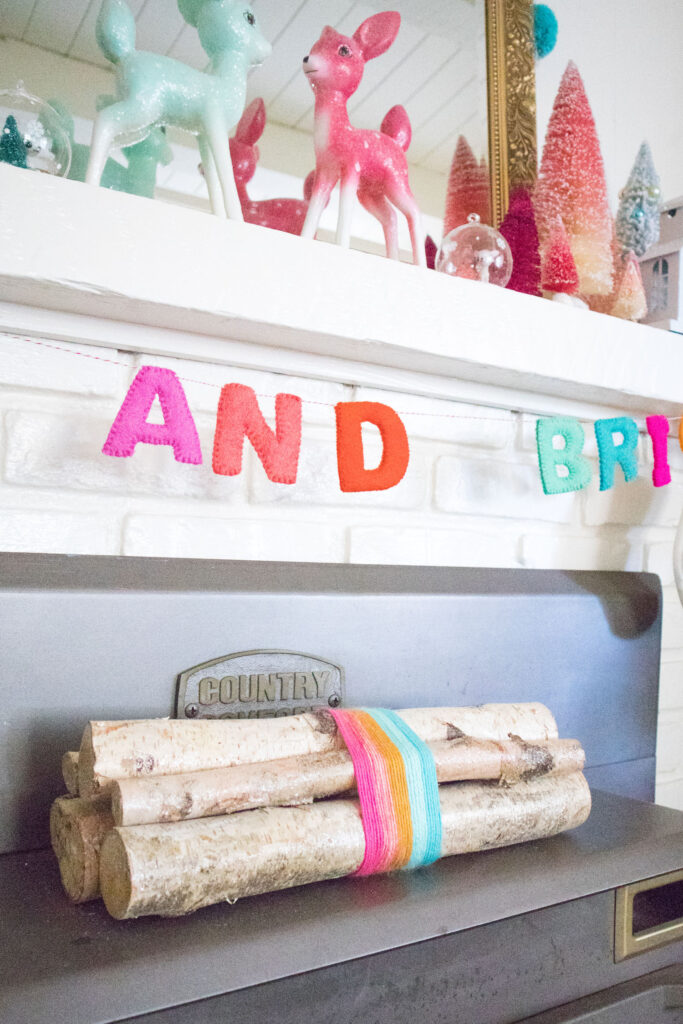 A bundle of glittery birch logs wrapped with colorful yarn. The bundle is placed on top of the fireplace.