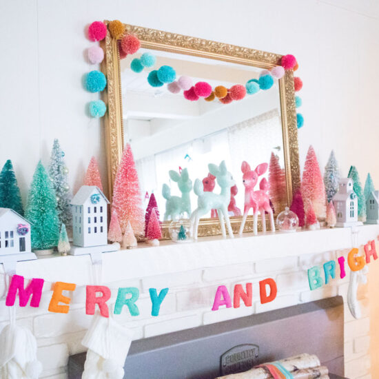 Side view of the fireplace mantel. The mantel is decorated with a large gold mirror, bottle brush trees, deer figurines and colorful garlands. Cream stockings are hung from stocking holders in the shape of houses.