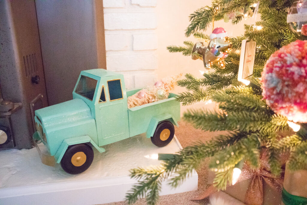 Mint metal truck placed on the fireplace hearth. It carries a bottle brush tree with mint and pink balls.