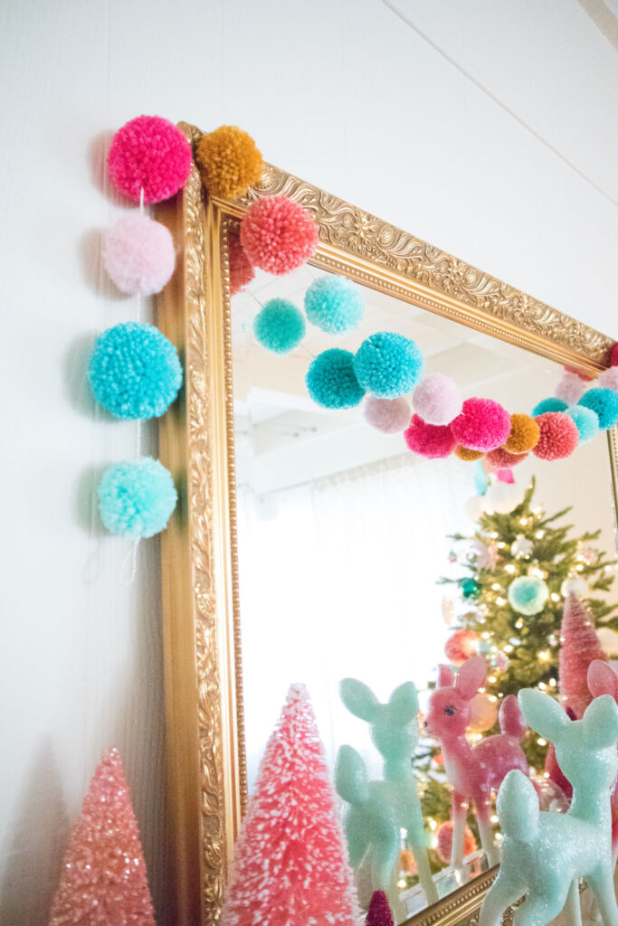 Pom pom garland made by Blaire from an assortment of colorful yarn. The garland is draped over the gold mirror.