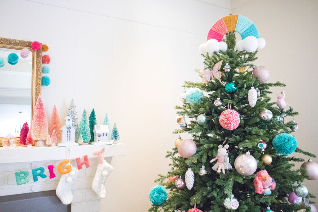 Blaire's colorful Christmas mantel and tree. The mantel is covered in colorful bottle brush trees, bright garlands and house stocking holders. The tree has a DIY rainbow tree topper, pom poms, and fun novelty ornaments.