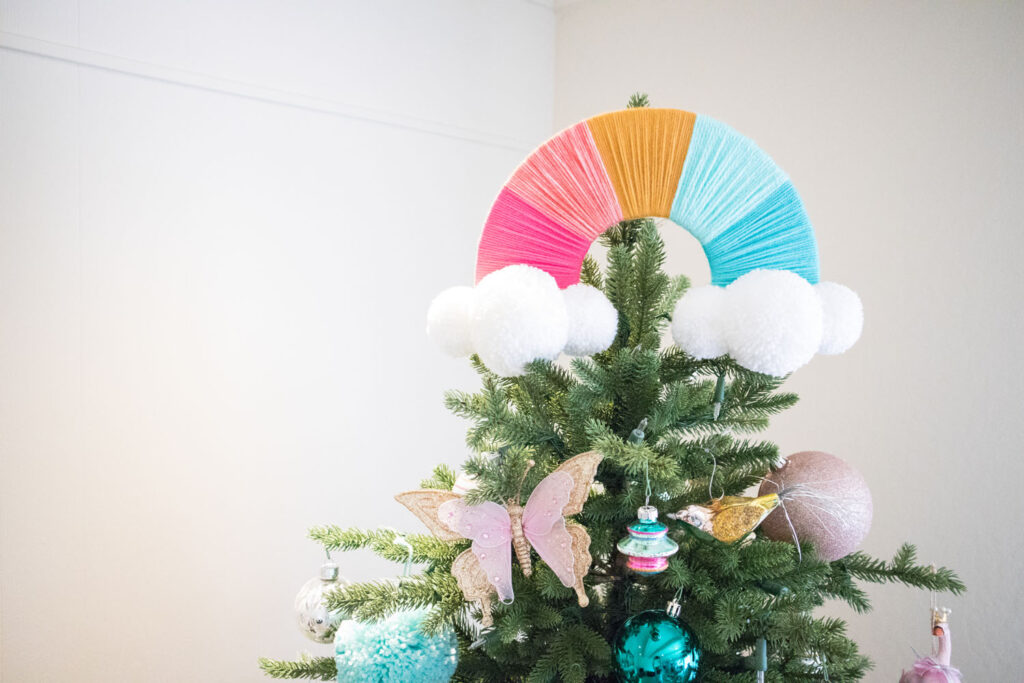 Close up of rainbow tree topper. It's made with 5 colors of yarn and white pom pom clouds.