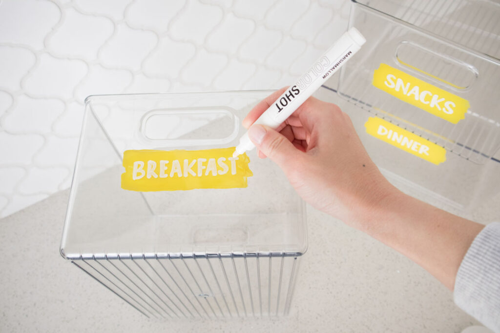 Writing "Breakfast" using Colorshot Marshmallow chalk marker on a clear bin with yellow painted label.
