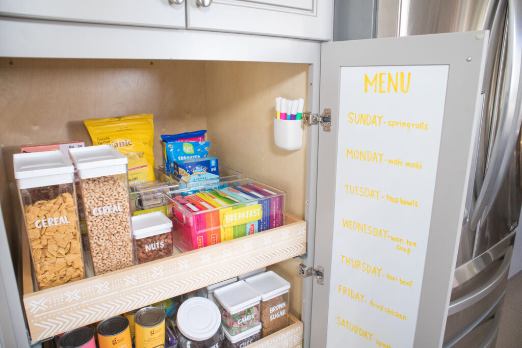 White chalkboard paper installed behind cabinet door. A menu is handwritten using Colorshot Emoji (yellow) chalk marker. A caddy holding chalk markers is mounted inside of the cabinet.