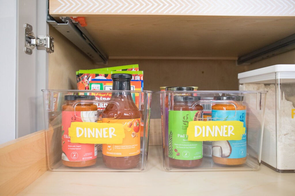 Photo demonstrating the arrangement of food items in rainbow order. There are two clear bins labeled "dinner" containing bottles with red, orange, green and blue labels.