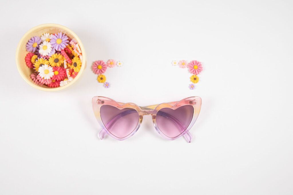 Plastic daisy charms are arranged above sunglasses.