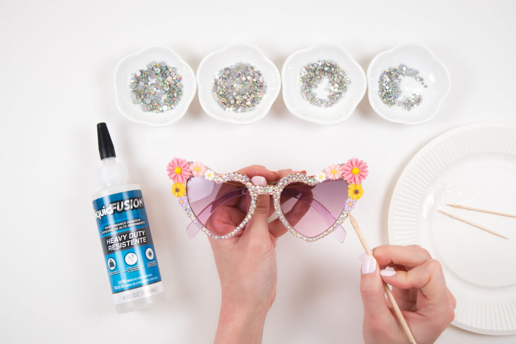 Blaire attaches rhinestones to the sunglasses by applying Liquid Fusion using a toothpick and using her rhinestone picker to pick up and apply rhinestones one by one.