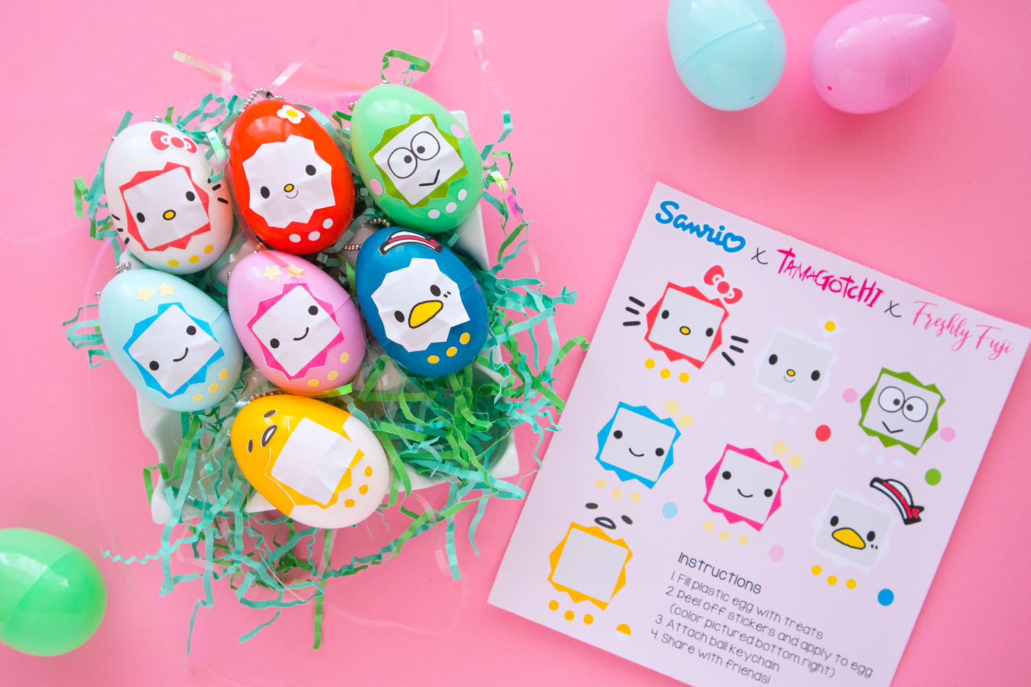 Overhead shot of Sanrio x Tamagotchi Inspired Easter Eggs. To the left is a ceramic egg carton filled with green Easter grass and 7 keychains (Hello Kitty, My Melody, Keroppi, Lala, Kiki, Tuxedo Sam, Gudetama). To the right is a sticker sheet that has the Sanrio characters faces.