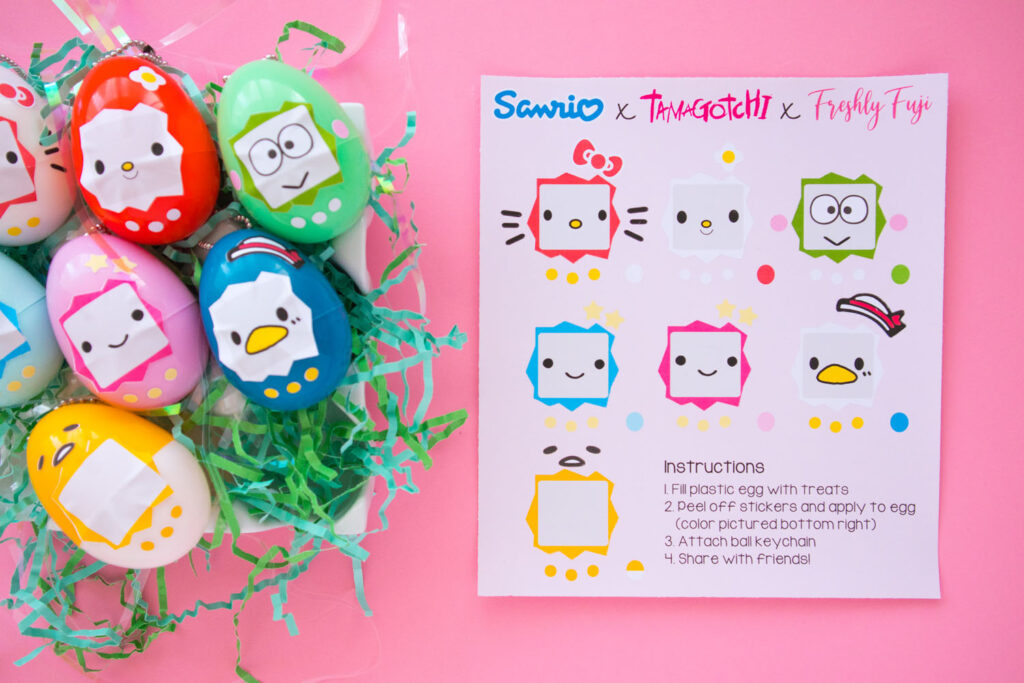 Overhead shot of Sanrio x Tamagotchi Inspired Easter Eggs. To the left is a ceramic egg carton filled with green Easter grass and 7 keychains (Hello Kitty, My Melody, Keroppi, Lala, Kiki, Tuxedo Sam, Gudetama). To the right is a sticker sheet that has the Sanrio characters faces.