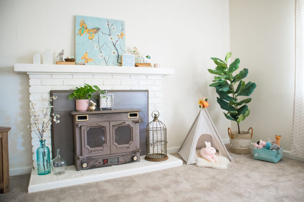 Spring living room inspiration. White brick mantel decorated for spring. Light blue canvas blossom art in center of mantel with other decorative elements.