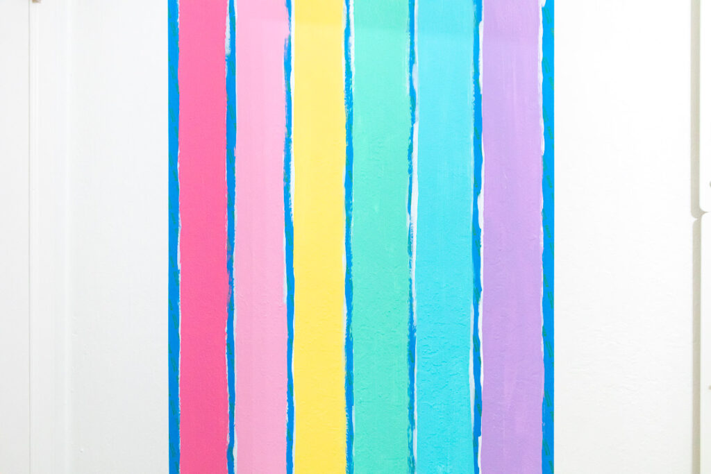 Close up of rainbow paint colors applied to the wall between painter's tape.