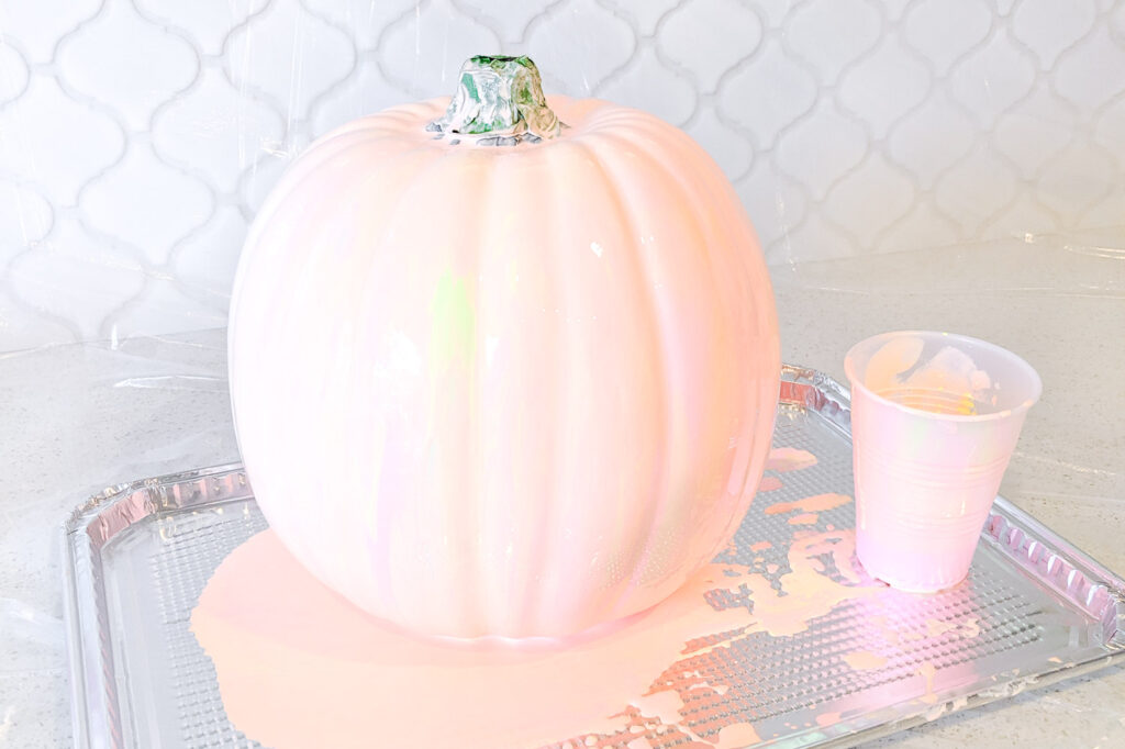Paint is poured on large pumpkin. It's now a marbled look with light pink, light orange and yellow paint.