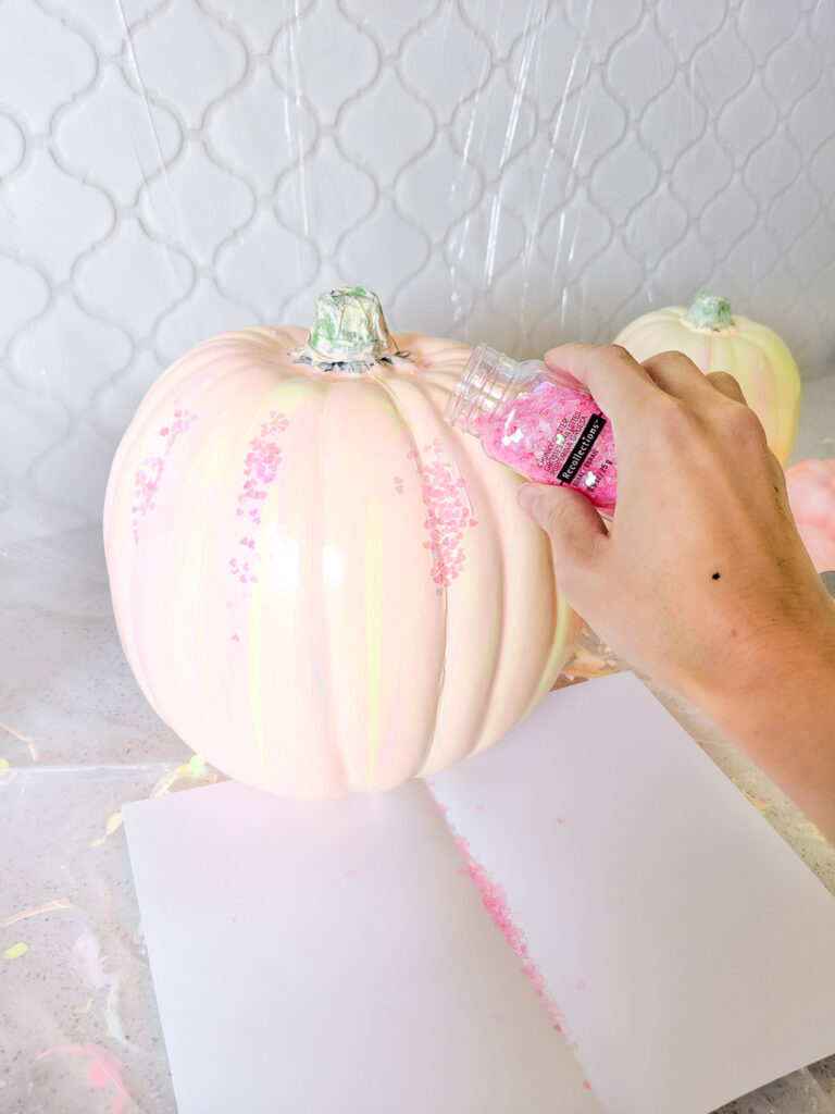 Sprinkling glitter onto the Mod Podge areas on paint pour pumpkins.
