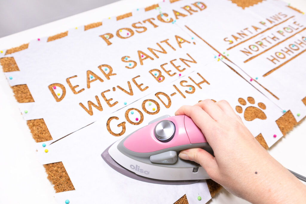 A small iron is placed on freezer paper stencil on top of doormat.