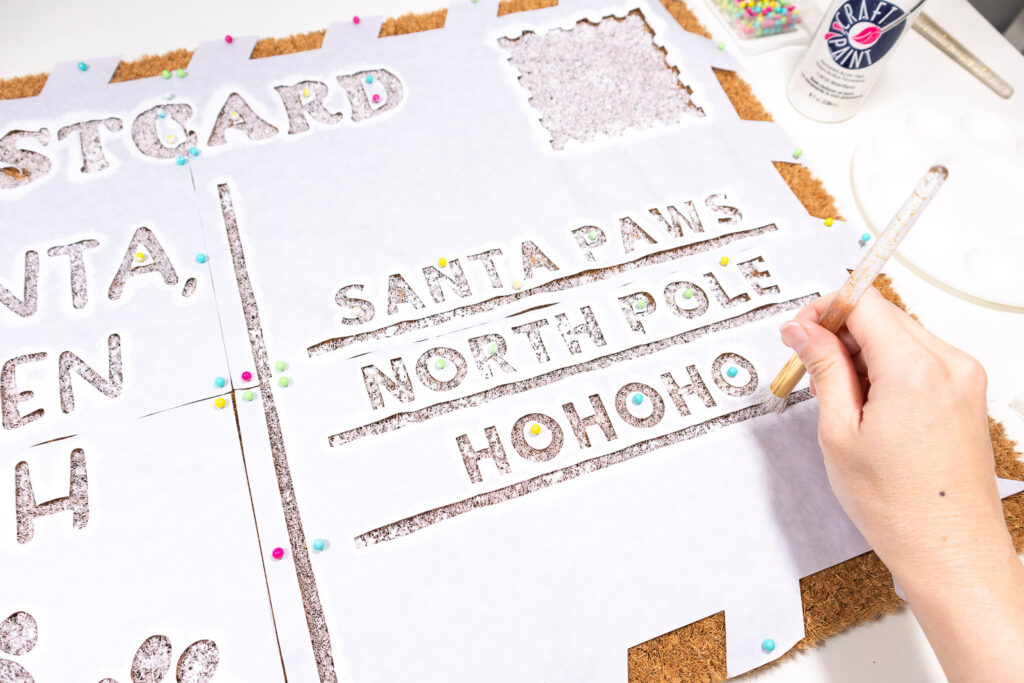 Using a stencil brush to apply white paint to the words of the postcard doormat.