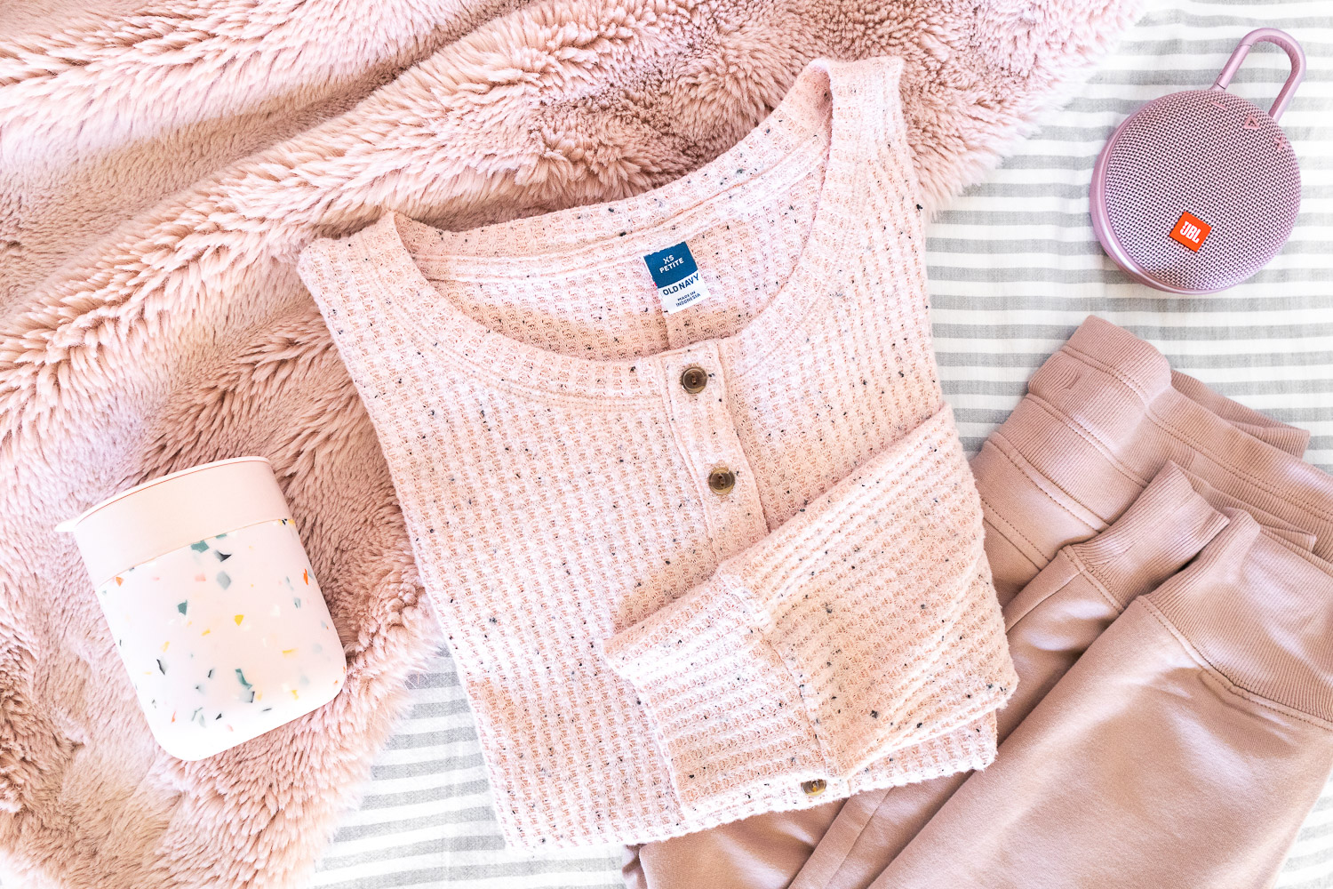 Blush pink loungewear, mug, portable speaker, and faux fur throw.