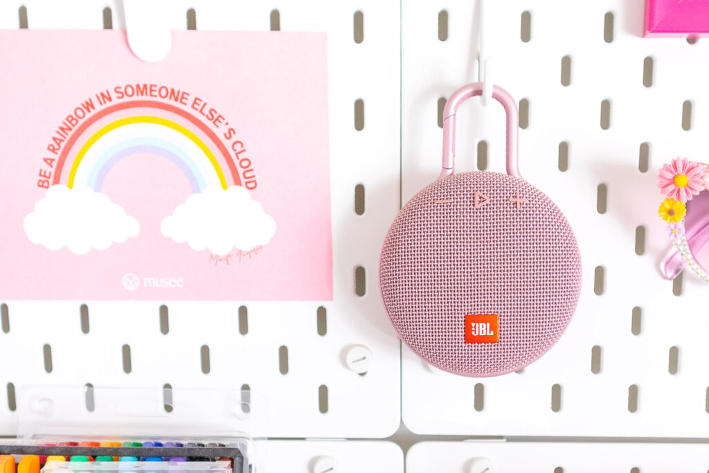 Pink portable speaker hanging on a craft room pegboard.