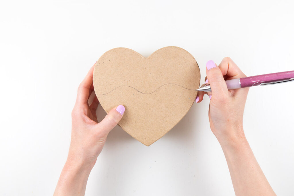 Drawing a wavy line across the top of heart paper mache box.