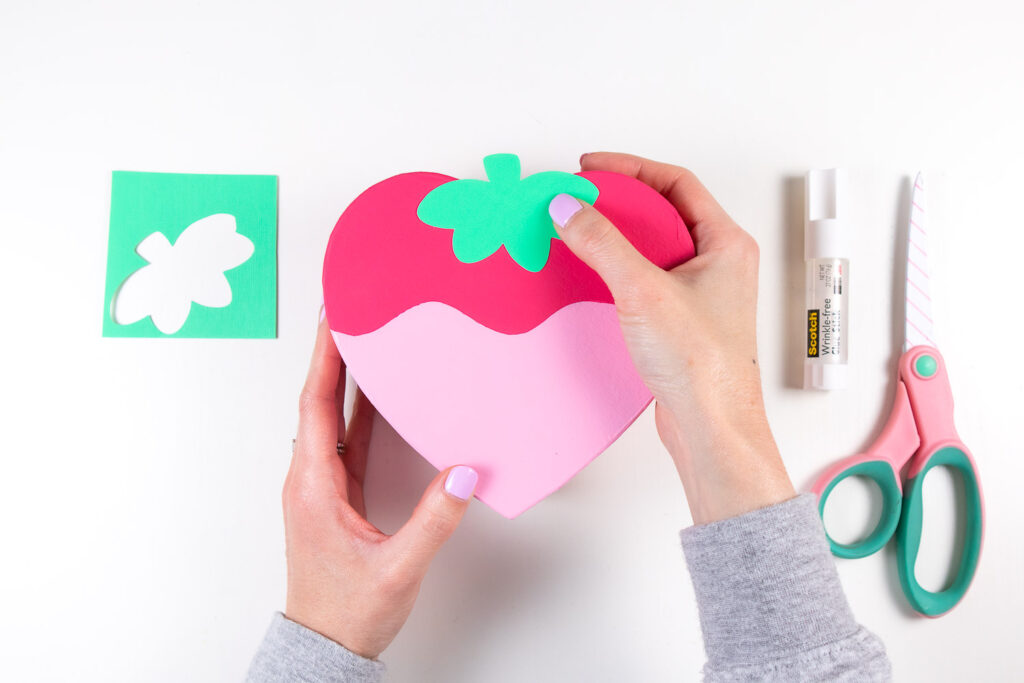 Placing green leaf cut out on the top of strawberry heart painted box.